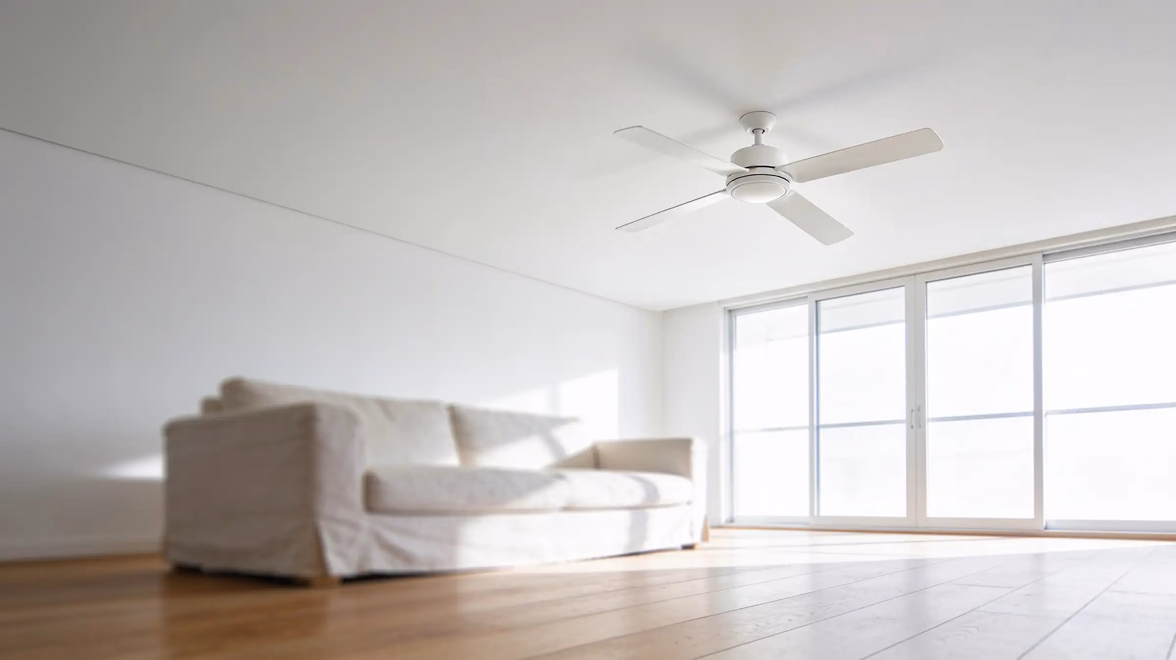 A white four-blade ceiling fan in a bright living room, a linen sofa on timber floors and sliding glass doors full of daylight